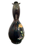 An ornate, dark glazed ceramic Art Nouveau vase with two handles and raised floral designs in yellow, purple, and green.