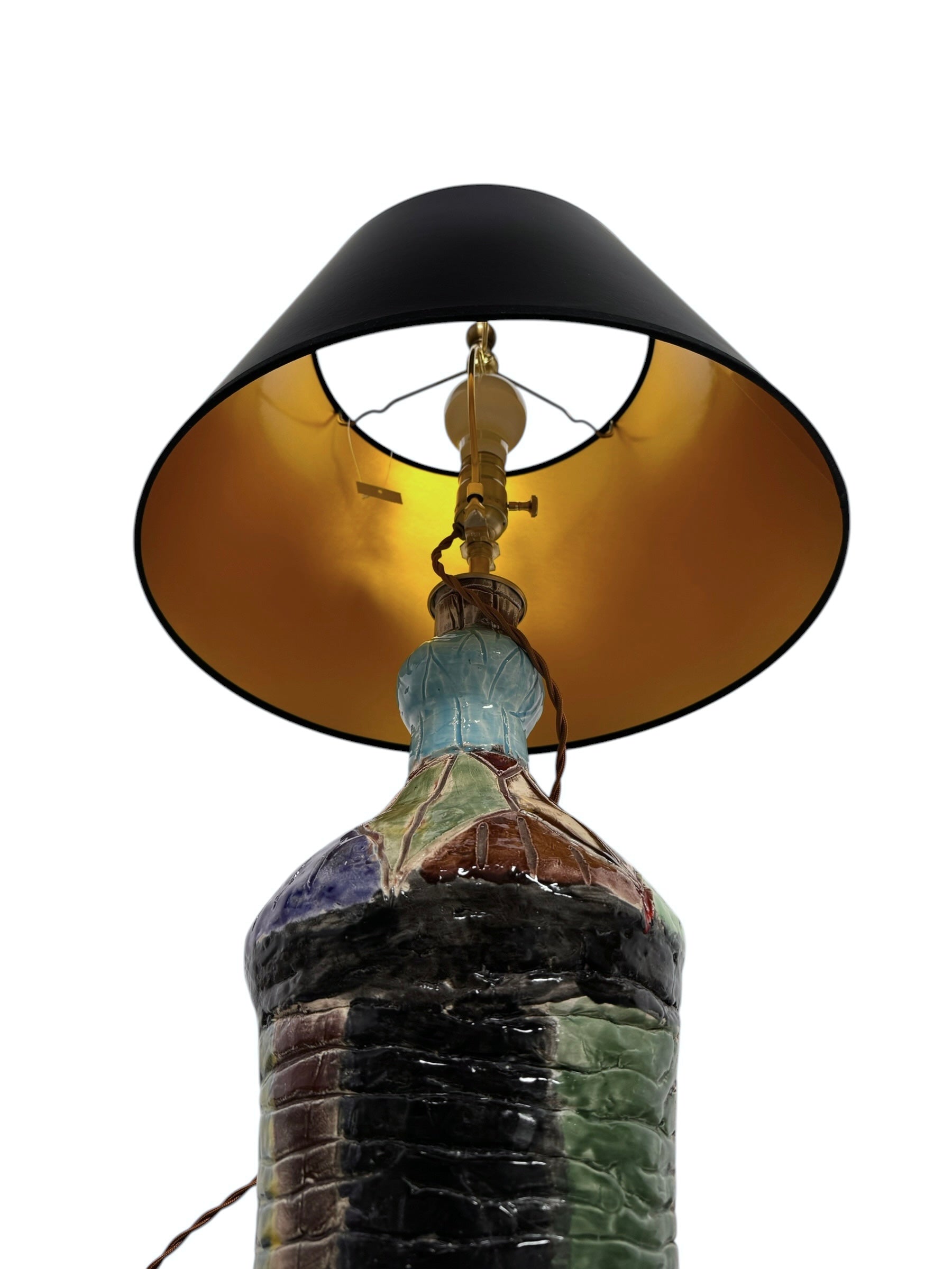 A hand-crafted ceramic table lamp featuring a vibrant, multi-colored base and a sleek black shade. The base is an upcycled artisan vase with a textured, hand-thrown appearance, decorated with geometric panels in shades of mustard yellow, forest green, cobalt blue, and burgundy, separated by thick black outlines. The lamp is topped with a minimalist, black tapered drum shade that provides a sharp contrast to the colorful, eclectic pottery below.
