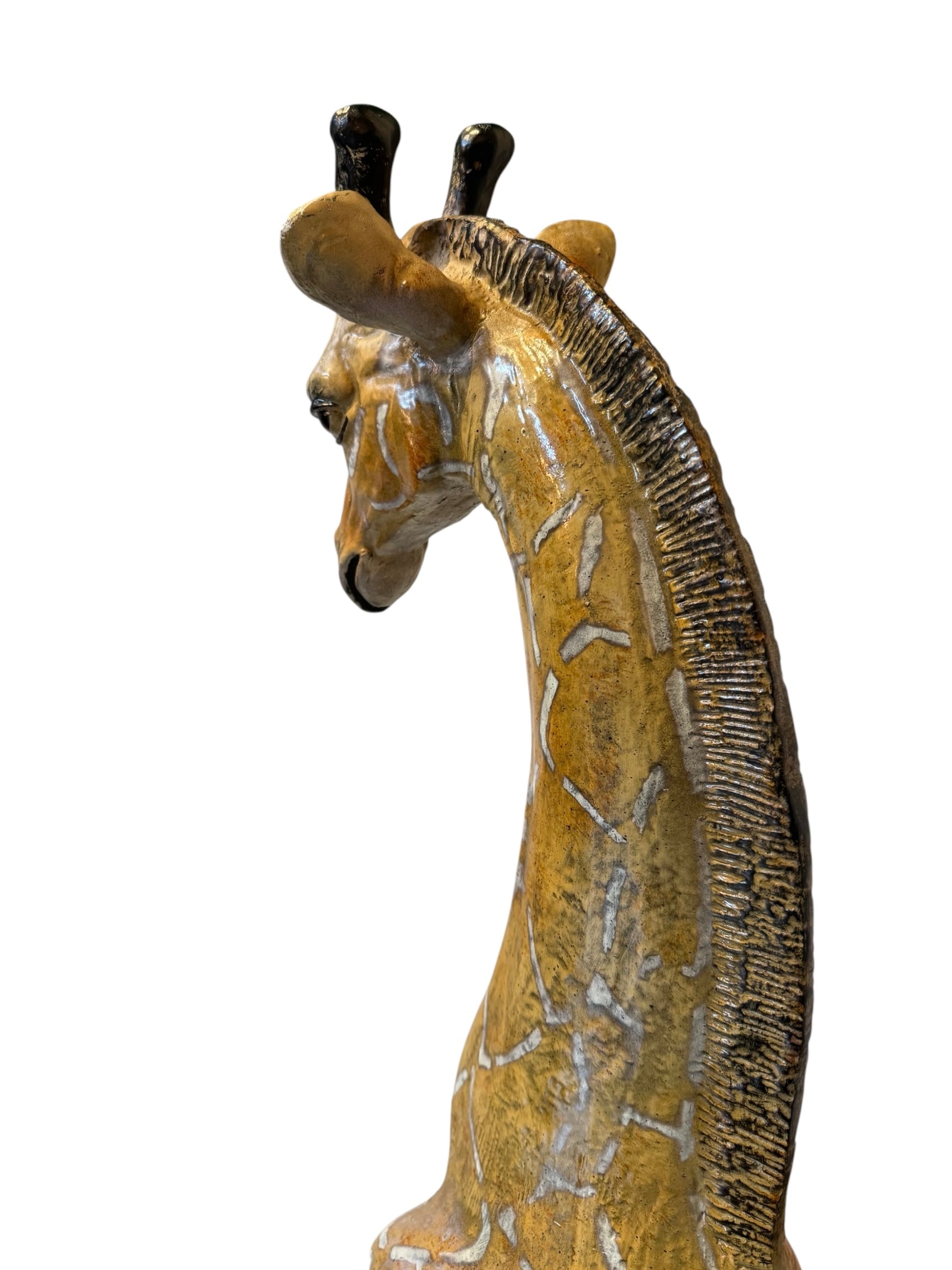 A hand-painted, cast resin sculpture of a seated giraffe. The giraffe has a long neck, is predominantly gold with light markings, and is in a resting pose. The sculpture is against a plain white background