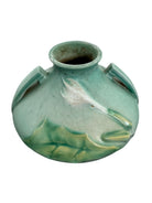 A squat, rounded vintage Roseville pottery vase in a light teal-blue matte glaze. The vase features two small, angular geometric handles on its shoulders and a flared rim. Embossed on the front is a cluster of textured, green and pale-yellow thornapple blossoms tucked against sharp, serrated green leaves. The surface shows a subtle, fine network of age-related crazing lines throughout the glaze.