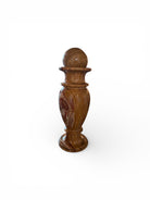 An elegant, hand-carved decorative vase made of polished Pakistani brown onyx. The vase features a classic, rounded urn shape with a tiered, flared neck and a solid matching spherical stone stopper resting on top. The stone displays rich, natural horizontal banding and swirling patterns in shades of honey, deep amber, rust-red, and cream. It stands on a small, integrated pedestal base against a clean white background, reflecting a high-gloss, mirror-like finish.