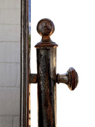 The antique Chevalier Mirror features a rectangular swing frame supported by two turned posts on decorative trestle feet. The mirror stands on four scrolled feet and features its original tarnished, silvered finish. The front of the mirror reflects a bright blue sky with wispy white clouds. The original dark brown backing is still attached to the frame.