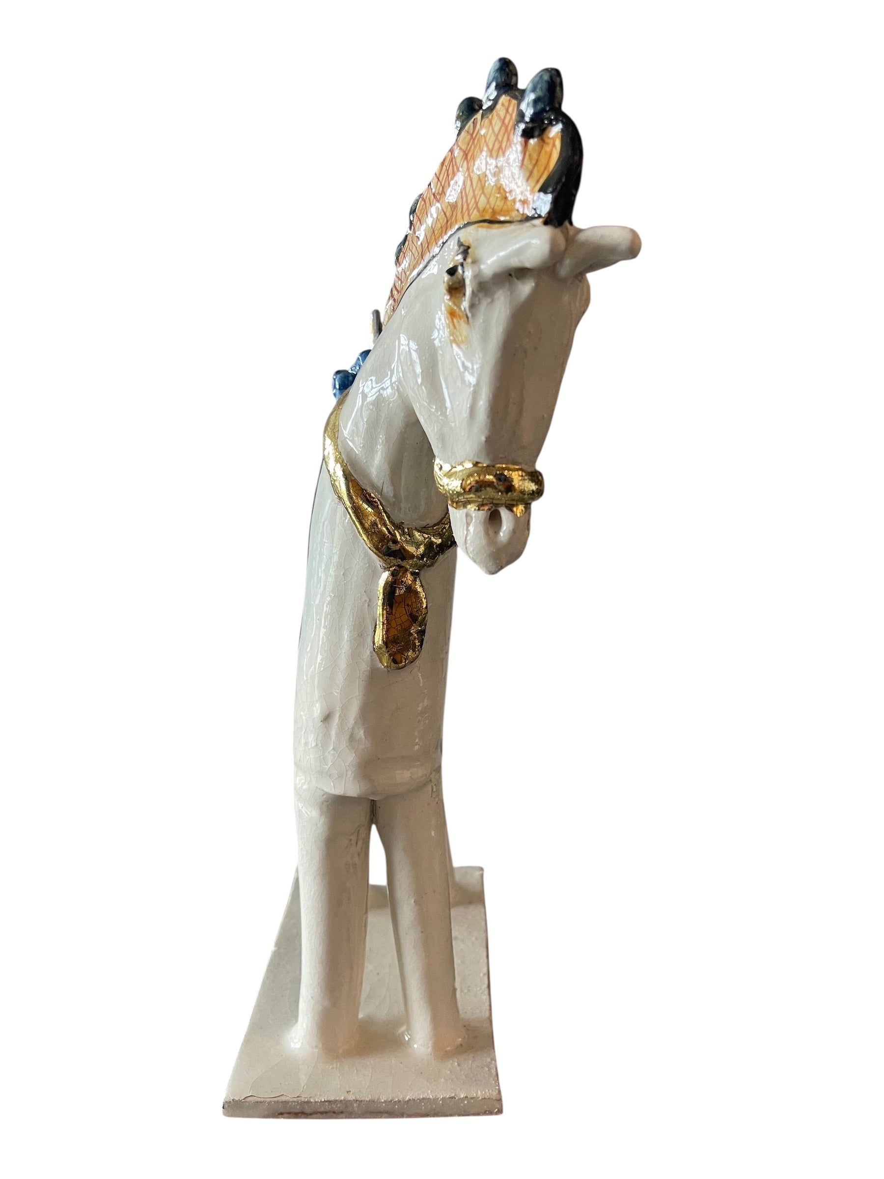 Ceramic horse by Domenico Pinto, featuring a white glazed body, geometric quilting on the saddle, gold accents, and 24Kt gold detailing. The horse stands on four legs and is placed on a white base.