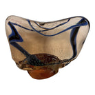 An asymmetrical Murano art glass sculpture with a heavy, biomorphic form. The piece is composed of thick, translucent smoky-amber glass with abstract, fluid bands of deep blue and dark brown swirling throughout the upper rim and sides. A dense pattern of tiny, controlled air bubbles is suspended inside the glass, concentrating heavily near the thick, solid amber base.