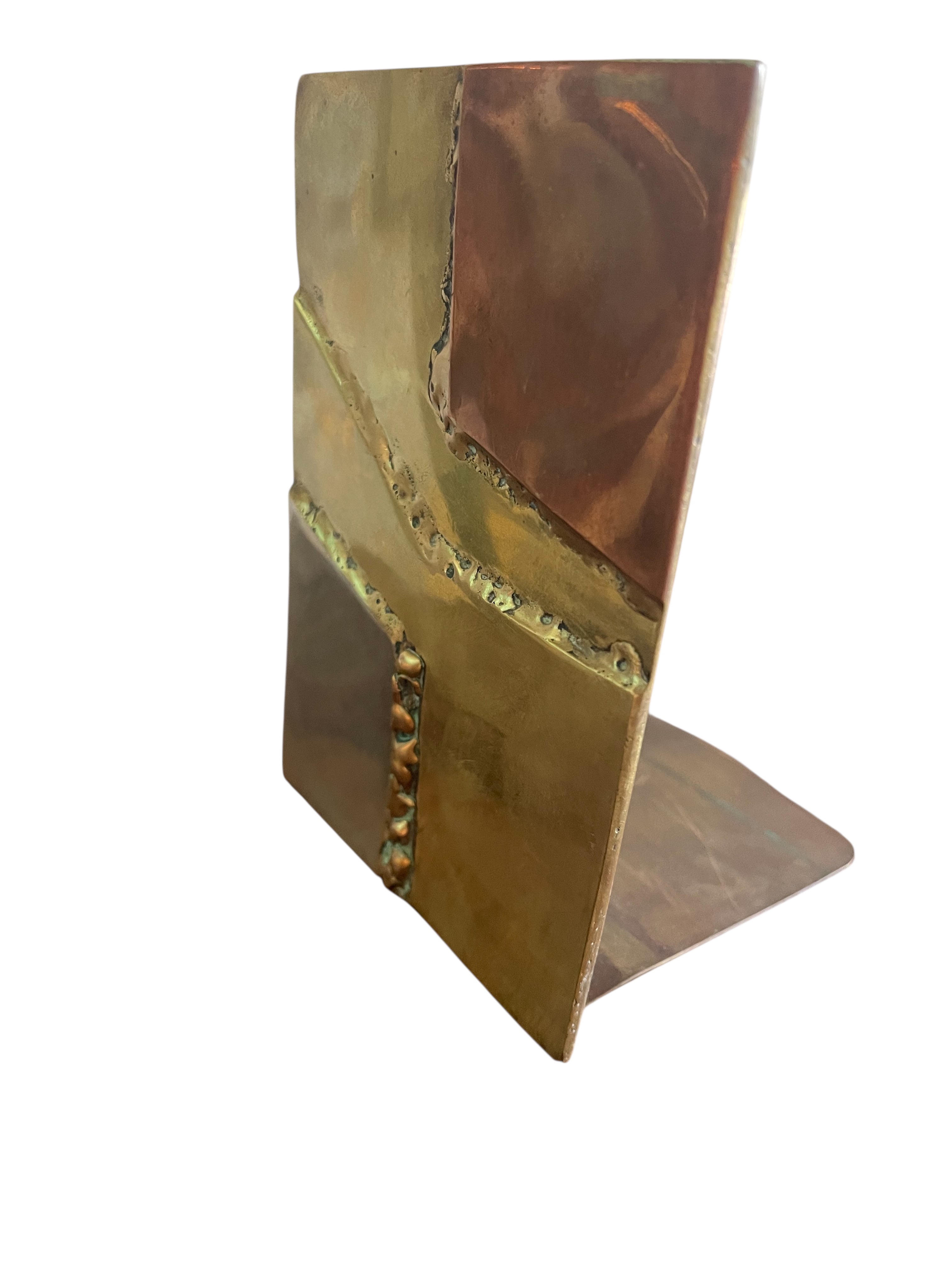 Close-up of two David Marshall Brutalist bookends. The bookends feature contrasting silver and bronze metal panels, separated by raised textured bronze seams. The bookends have a rough, geometric design.