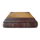 A vintage leather ledger book with metal hinges and spine, featuring text on the cover.